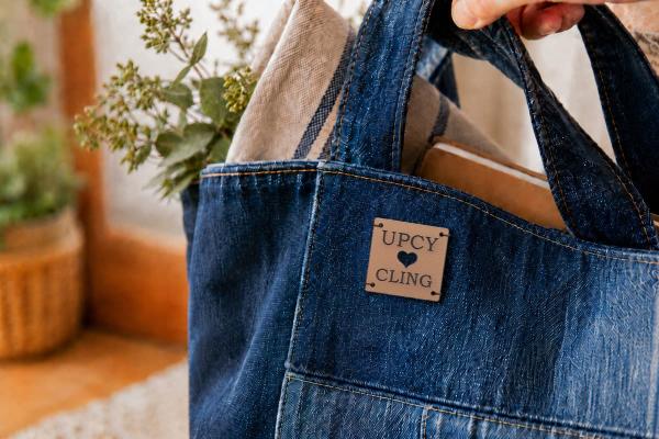 Etichetta quadrata in pelle di cactus chiara con "UPCYCLING" e cuore fustellato su borsa denim.